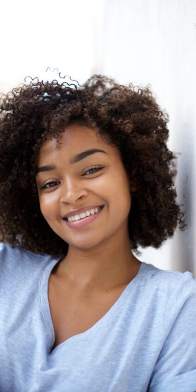 Close up portrait of smiling young african american woman leaning against wall outside